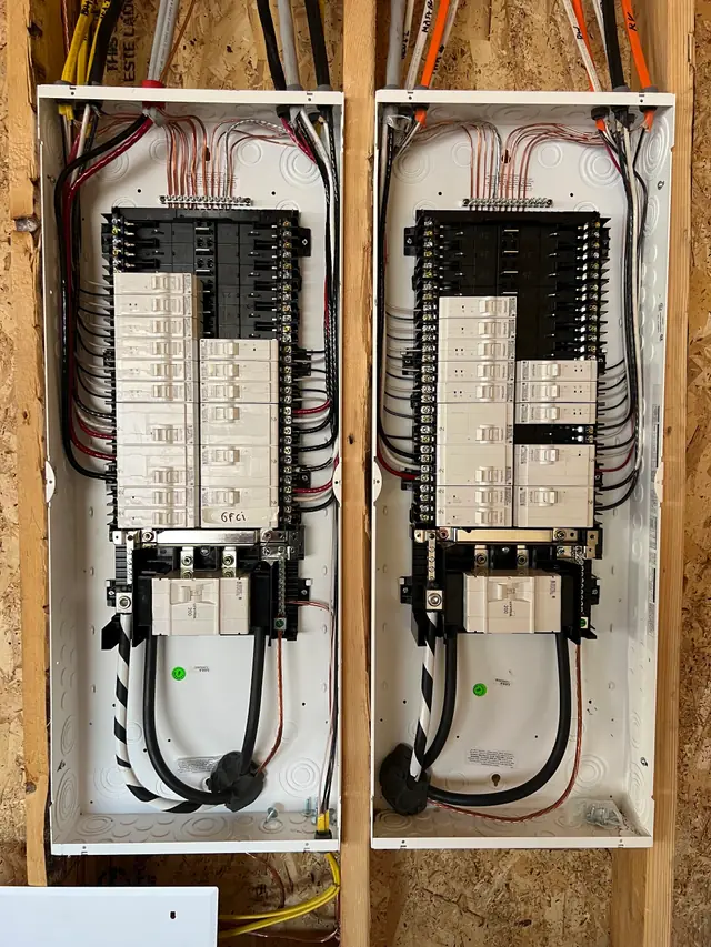 Two new electrical panels side by side in an open stud wall during rough-in