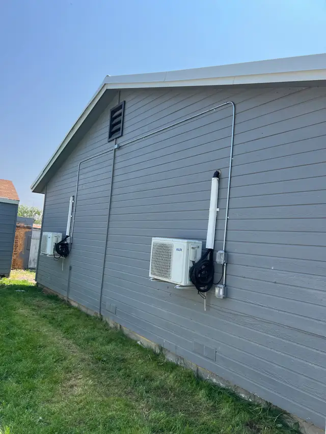 A mini-split condenser with its disconnect and a surface conduit run on grey siding