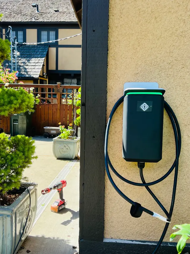 A wall-mounted EV charger on a stucco post beside a garden courtyard